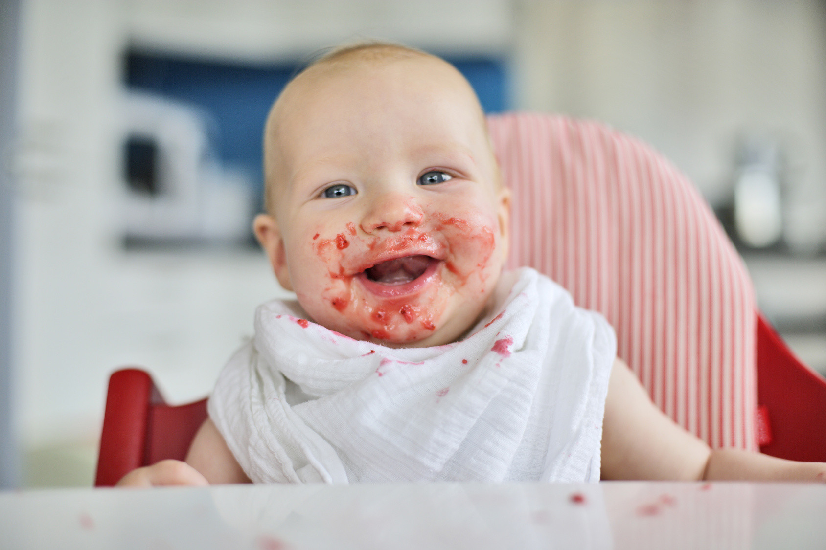 Baby mit Brei um den Mund lacht in die Kamera