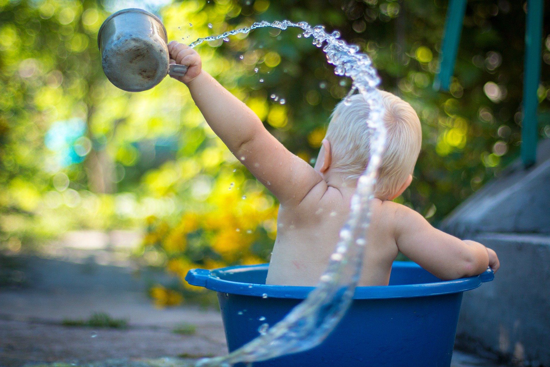 Thema Babypflege: Baby sitzt in einer Wanne und spritzt mit Wasser